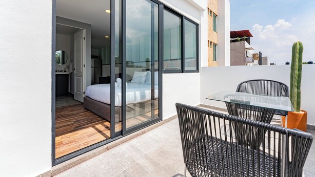 A modern balcony with a glass door leading to a bedroom, a dining area with a table and chairs, and a potted cactus. - Loft con terraza en CDMX (Narvarte) (Ciudad de mexico)