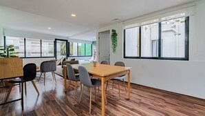 A modern dining area with a wooden table and chairs, large windows with blinds, and a view of the street. - Loft con terraza en CDMX (Narvarte) (Ciudad de mexico)