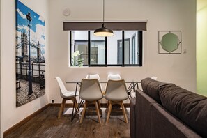 Un comedor con una mesa, cuatro sillas, una lámpara colgante, un ventanal grande y una obra de arte en la pared.