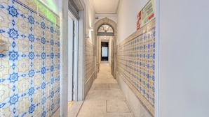 A corridor with patterned tile walls and a tiled floor, leading to a door. - FindMe inPorto Bonfim 0T (Porto)