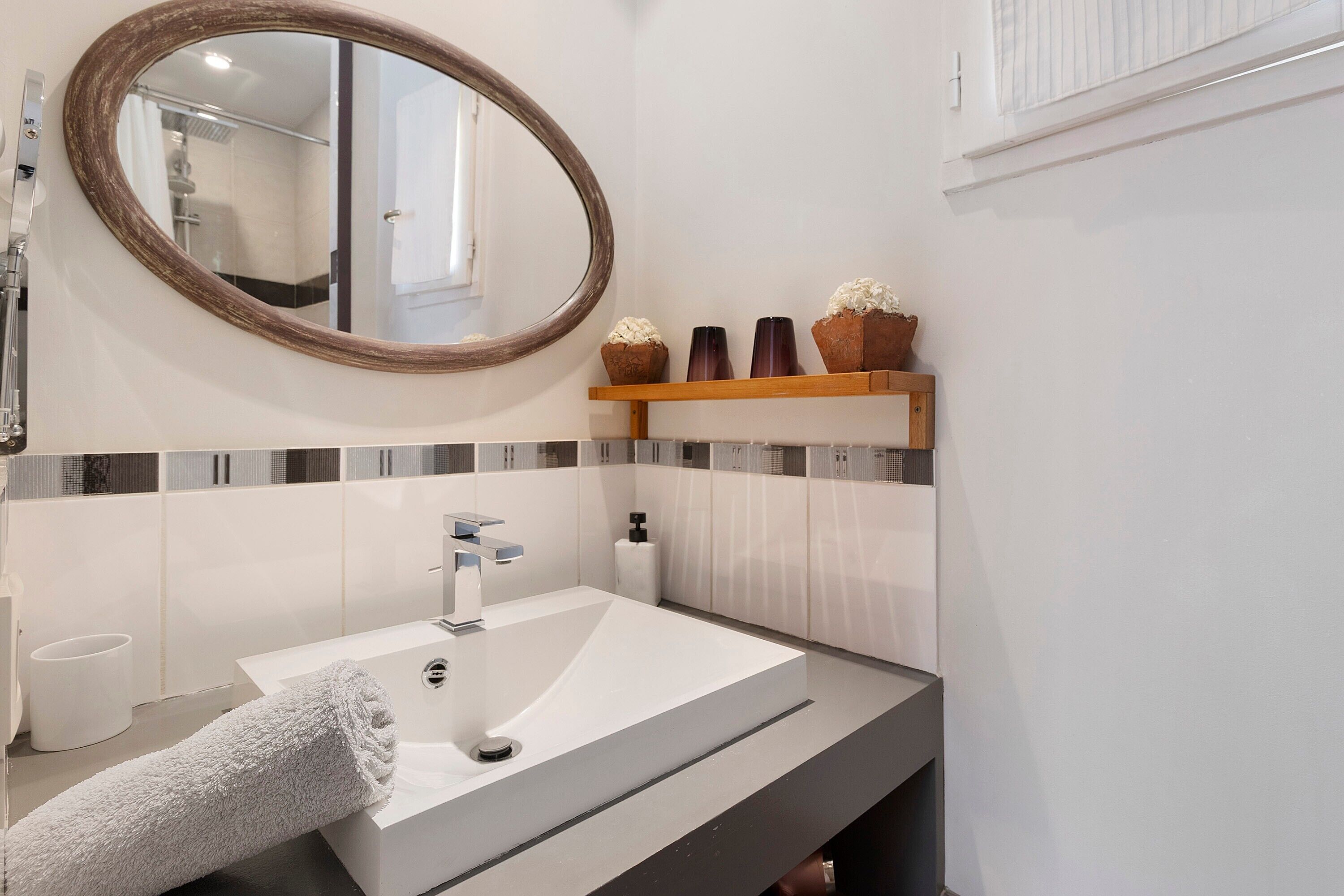 Een badkamer met een wit wastafel, een spiegel en een plank met decoratieve objecten.