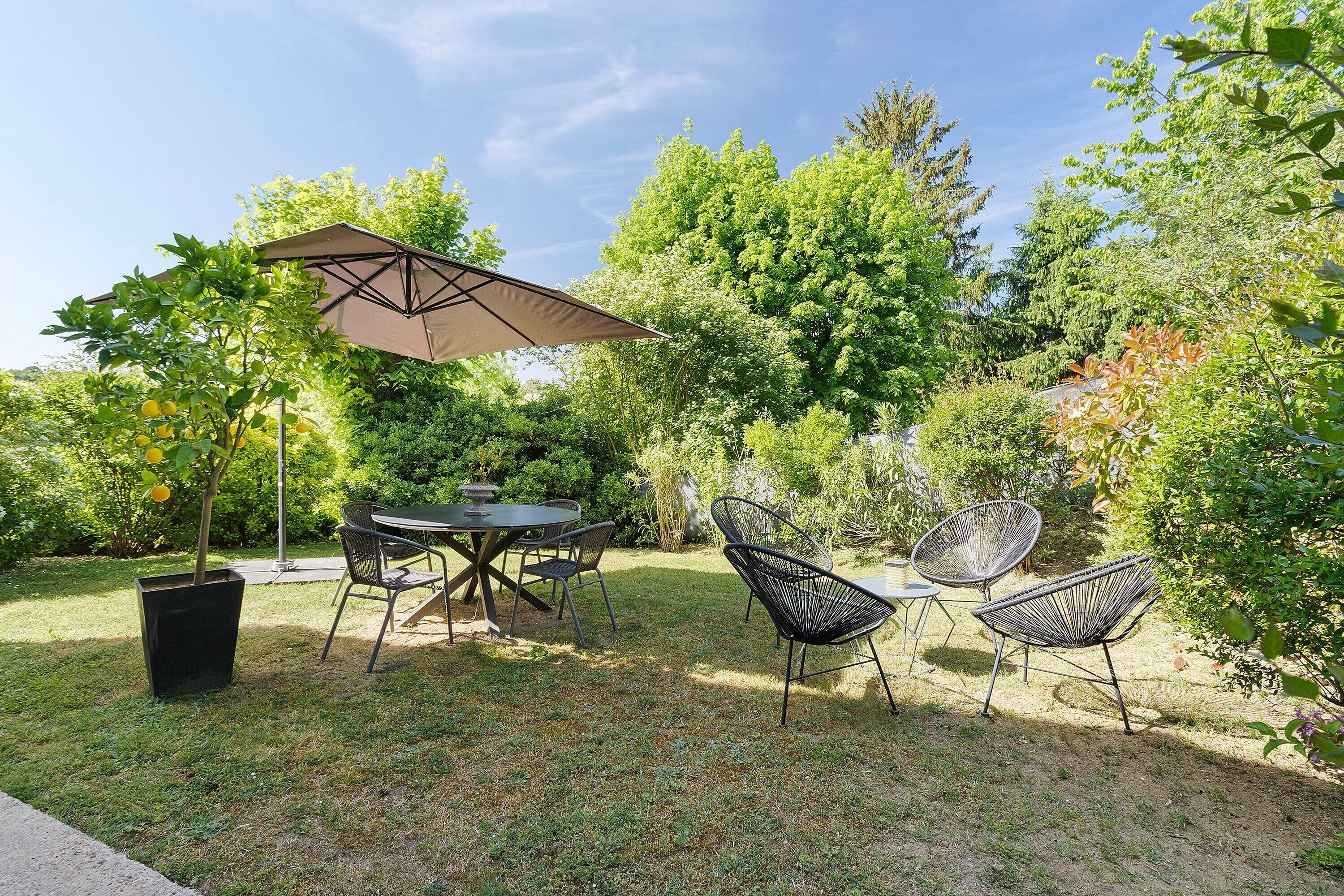 An outdoor patio with a table and chairs, surrounded by greenery and trees.