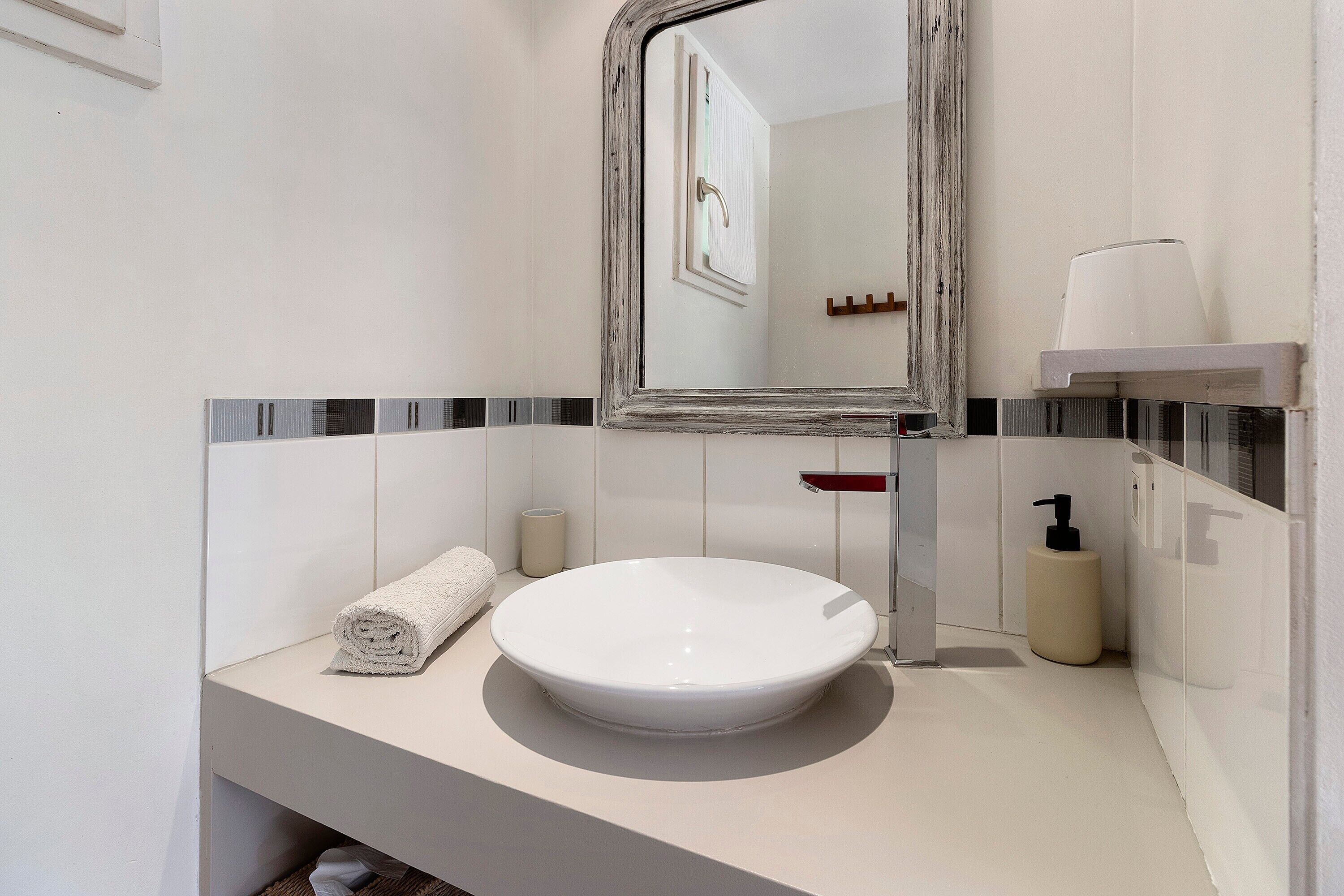 A bathroom with a white sink, a mirror, a towel, a soap dispenser, and a toilet paper holder.