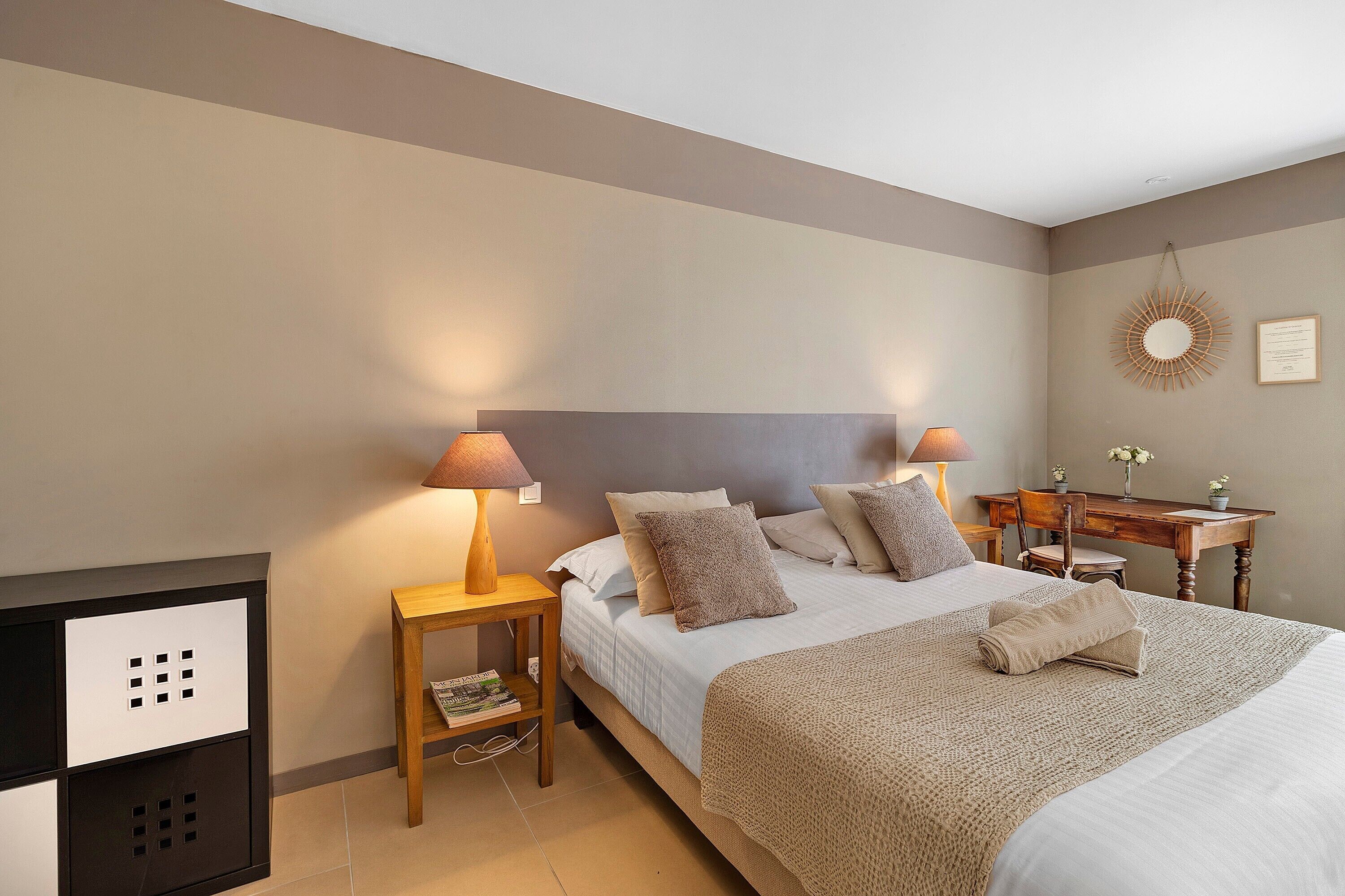 A neatly arranged bedroom with a bed, bedside tables, a desk, and a wall-mounted mirror.