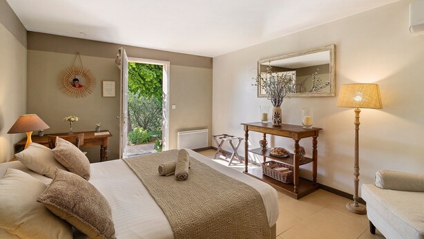 Ein Schlafzimmer mit Bett, Nachttisch, Lampe, Spiegel und Blick ins Freie.