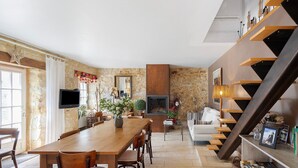 Ein Essbereich mit Holztisch und Stühlen, einem Kamin und einer Treppe mit Regalen.
