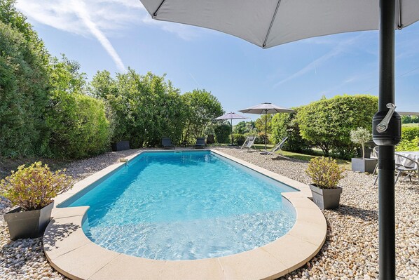 A swimming pool with a surrounding pebble area, a lounge chair, and a potted plant.