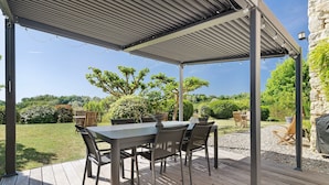 Une terrasse extérieure avec une table et des chaises abritées, entourée d’un jardin.