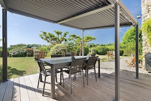 Un patio al aire libre con una mesa y sillas cubiertas, rodeado de un jardín.