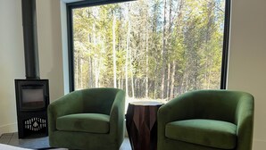 Una stanza con un letto, due poltrone verdi, un piccolo tavolo di legno e una stufa a legna.