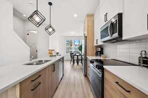 A modern kitchen with wooden cabinets, stainless steel appliances, and pendant lighting. - Rooftop Patio | King Bed | 2 Ensuites + Garage (Calgary)