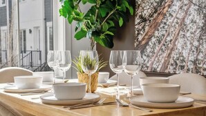 Ein Esszimmertisch mit weißen Schüsseln, Tellern und Weingläsern, dazu ein Korb mit Grünpflanzen.