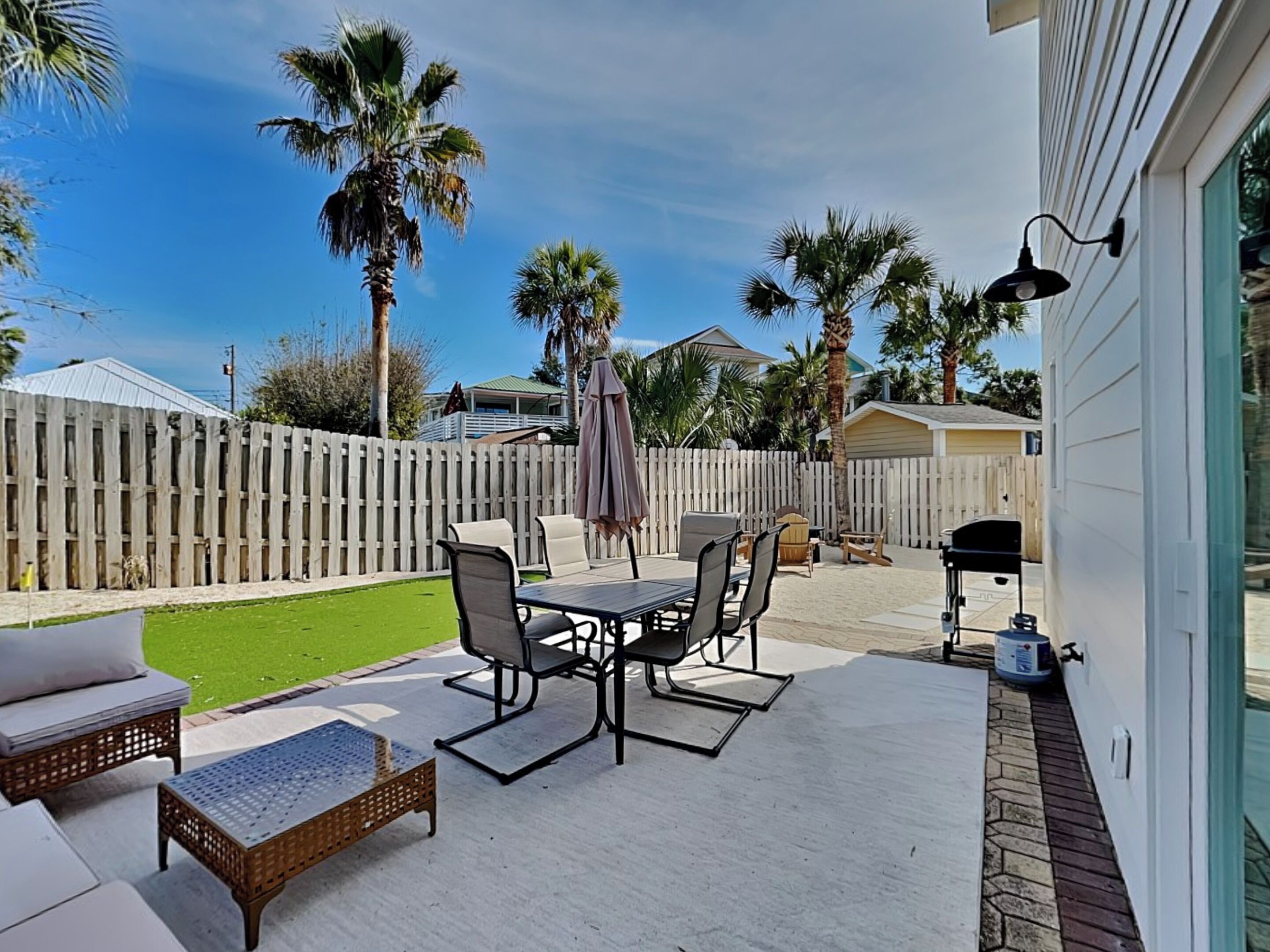 Un patio con mobiliario exterior, una parrilla y una valla blanca.