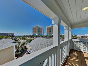 A balcony with a view of a hotel complex, palm trees, and a clear sky. - The Shore Thing (Panama City Beach)