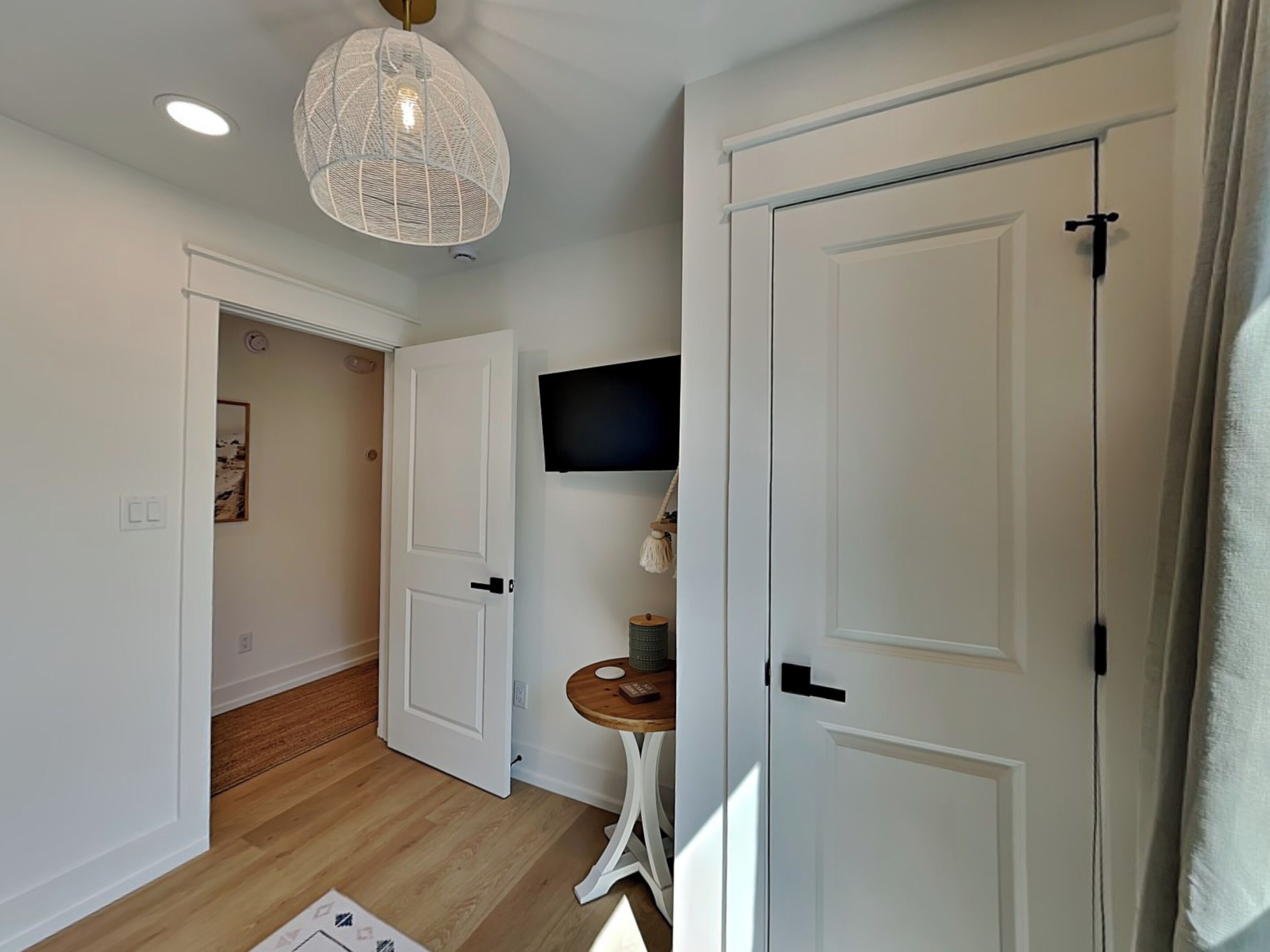 Un couloir avec des portes blanches, un plancher en bois, un luminaire au plafond et une petite table sur laquelle est posée une plante.