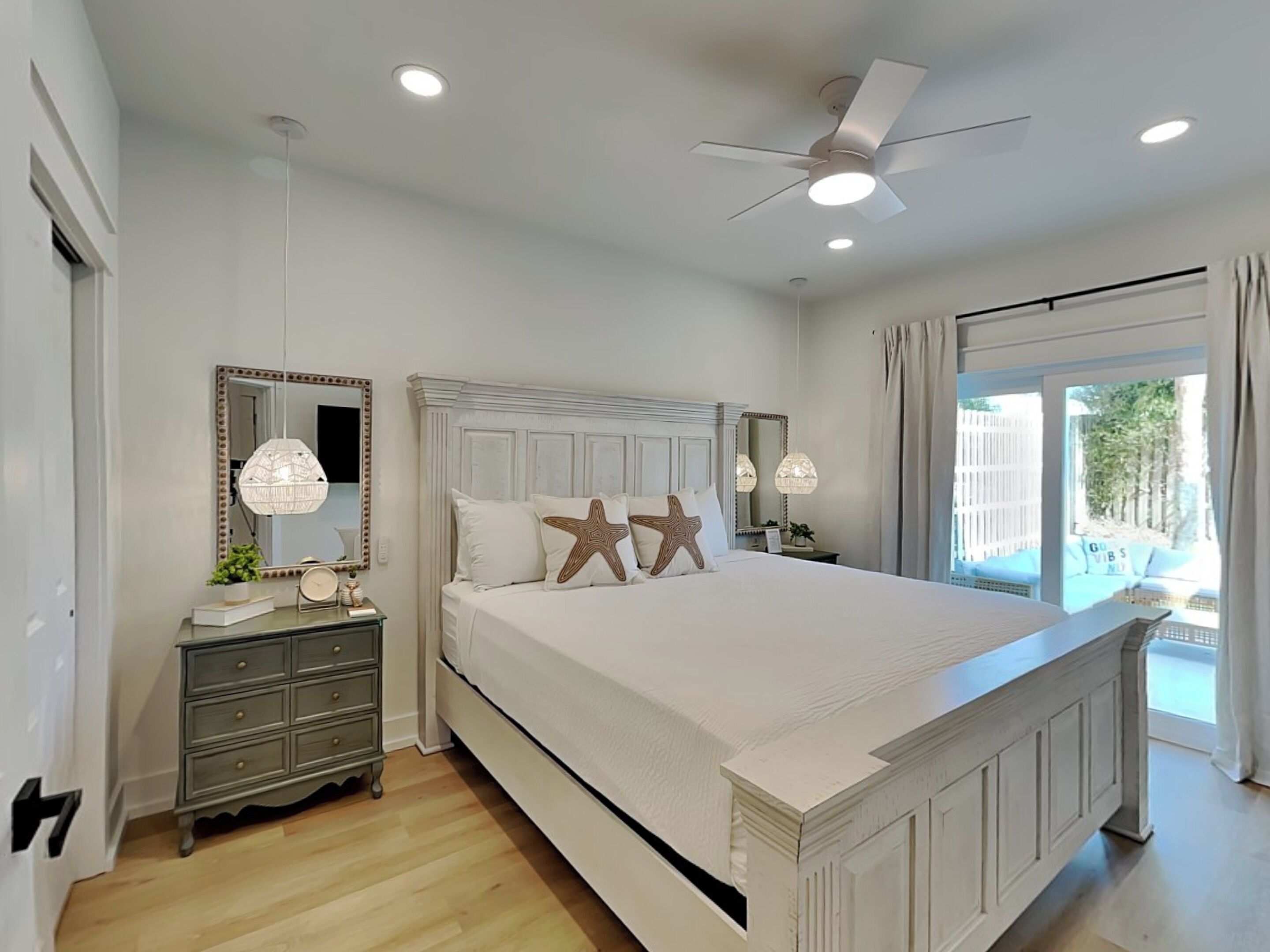 A bedroom with a large bed, two bedside tables, a ceiling fan, and a window with curtains.