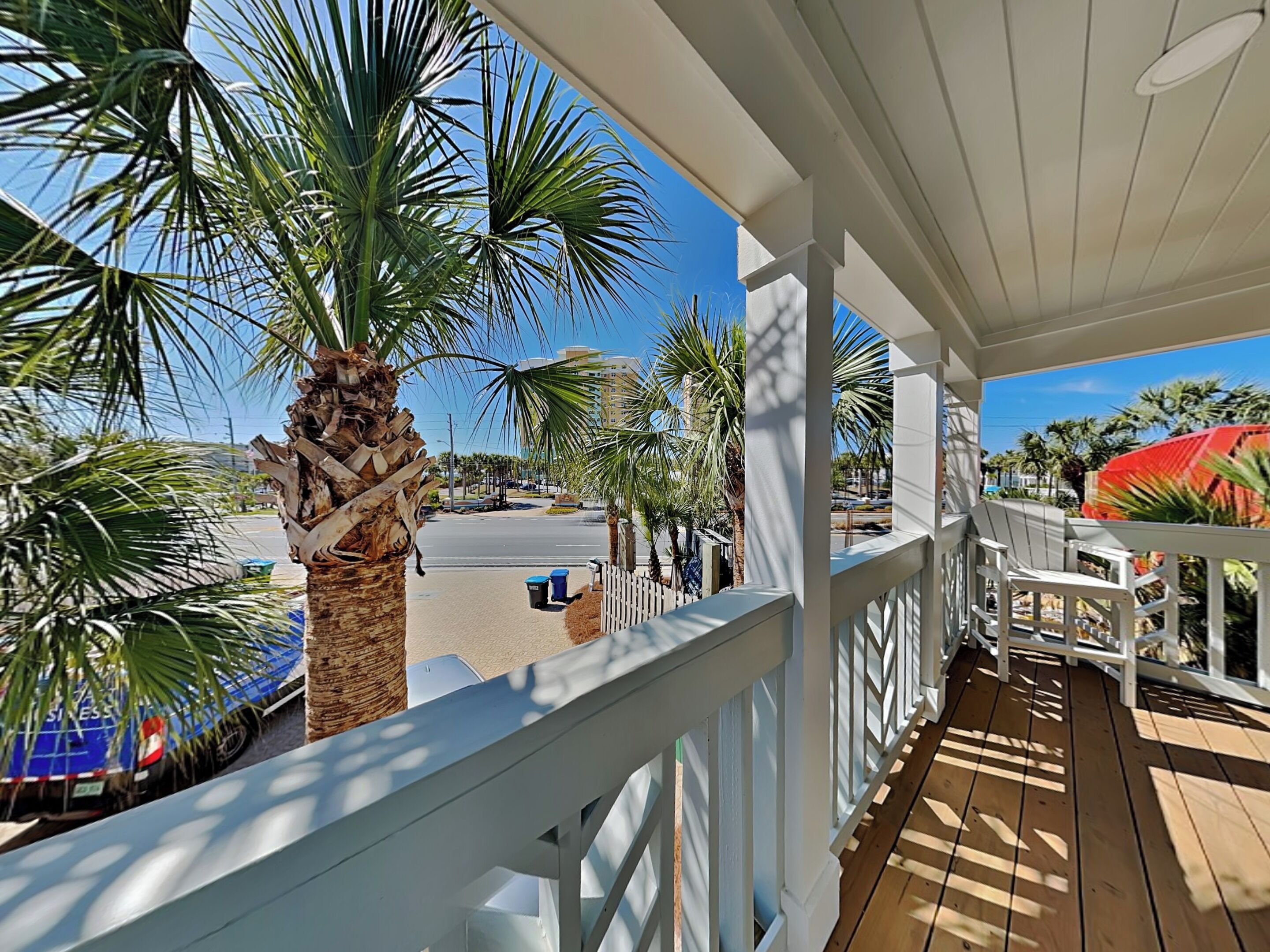 A balcony with a view of palm trees, a white railing, and a wooden deck.