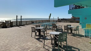 Een terras aan het strand met tafels en stoelen, een houten hek en uitzicht op de oceaan.