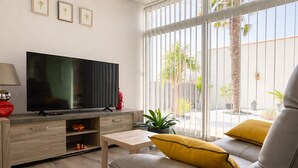 Ein modernes Wohnzimmer mit Flachbildfernseher, einer gelb gekissenen Couch, einem Couchtisch und einem Topf mit Pflanze.