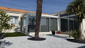 Ein modernes Haus mit großem Glasfenster, einer Palme und einer Schotterauffahrt.