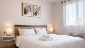 Ein ordentlich bezogenes Bett mit weißen Leinen, zwei Nachttische mit Lampen und zwei gerahmte Kunstwerke an der Wand.