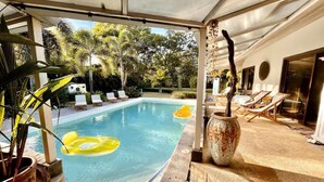 A covered pool area with lounge chairs, a potted plant, and a decorative vase. - Spacious Jungle Villa nr Tamarindo w big pool - Perfect for Retreats (Tamarindo)