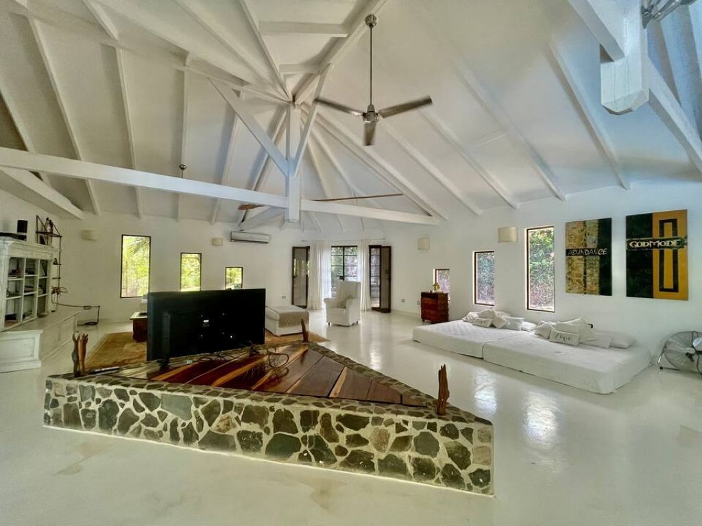 A spacious living area with a stone fireplace, white sofas, and a ceiling fan.