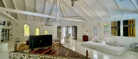 A spacious living area with a stone fireplace, white sofas, and a ceiling fan.