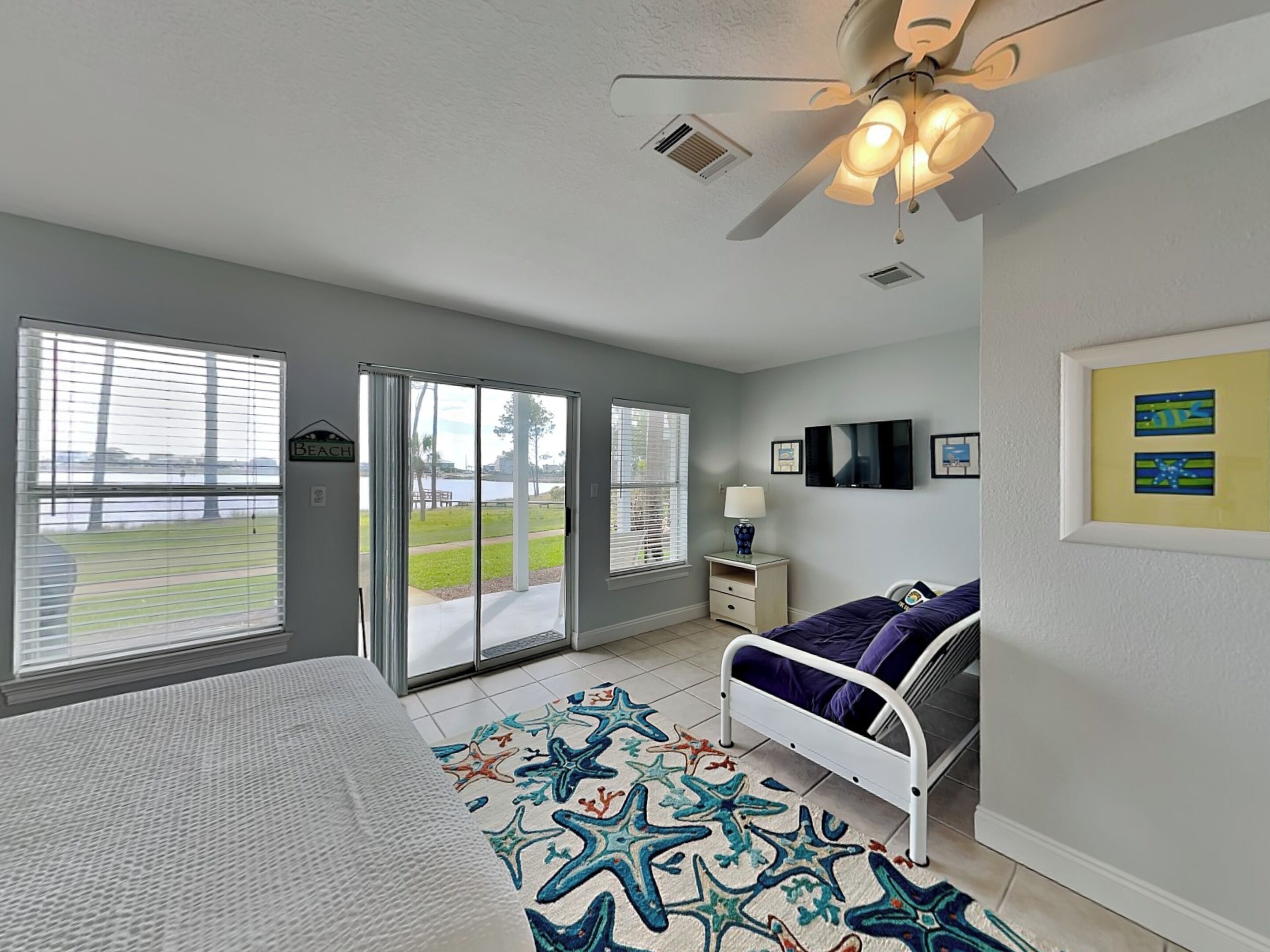 A bedroom with a bed, a ceiling fan, a TV, and a view of a park through the window.