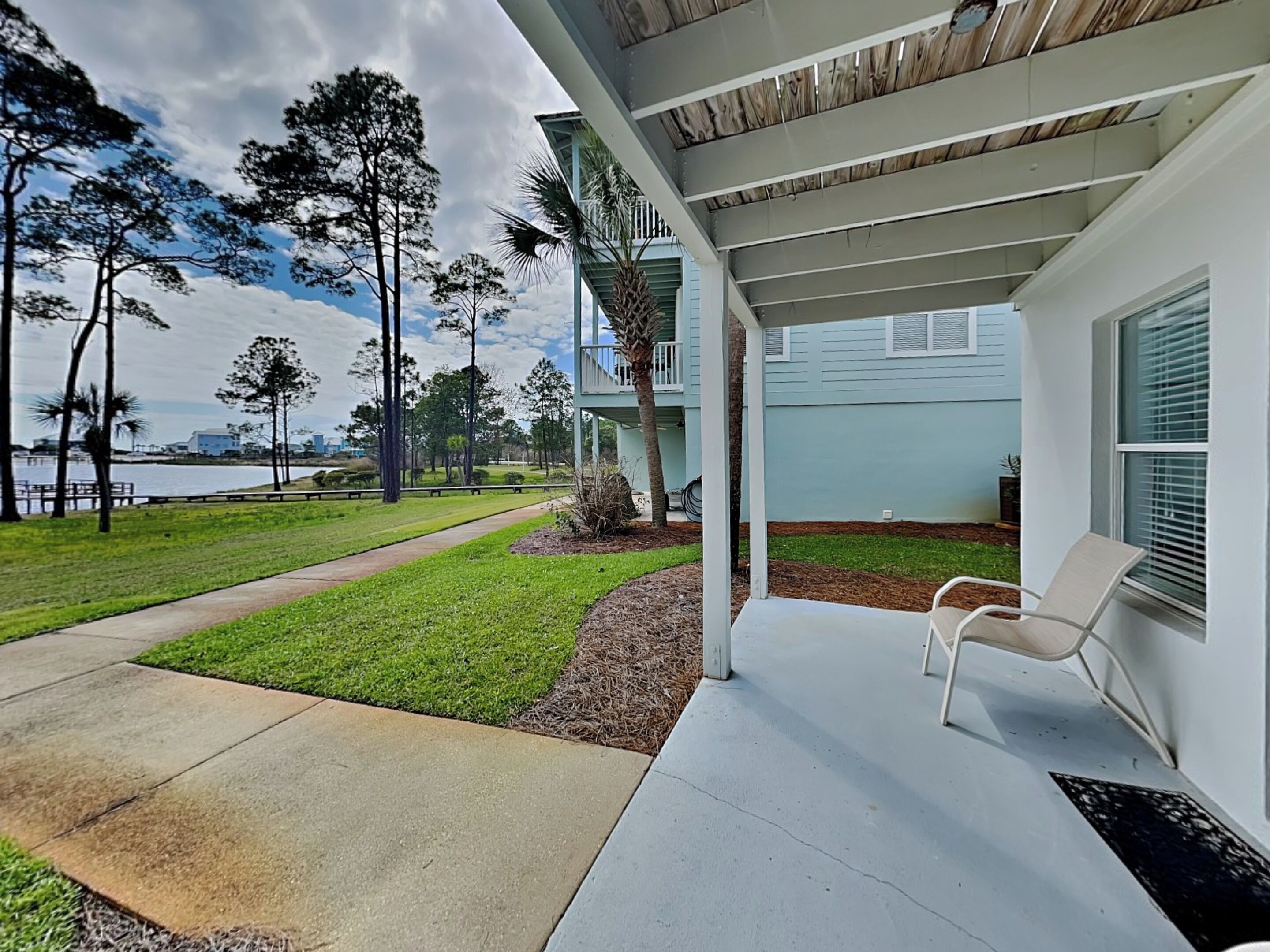 A covered patio with a chair, a concrete path, and a view of a body of water and trees.