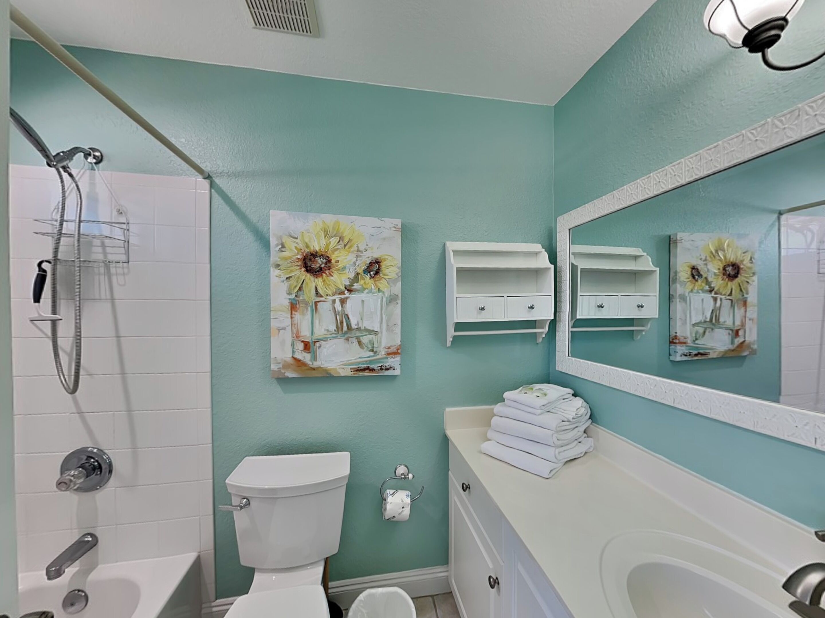A bathroom with a white toilet, a shower with a handheld showerhead, a sink with a mirror, and a wall-mounted towel rack.