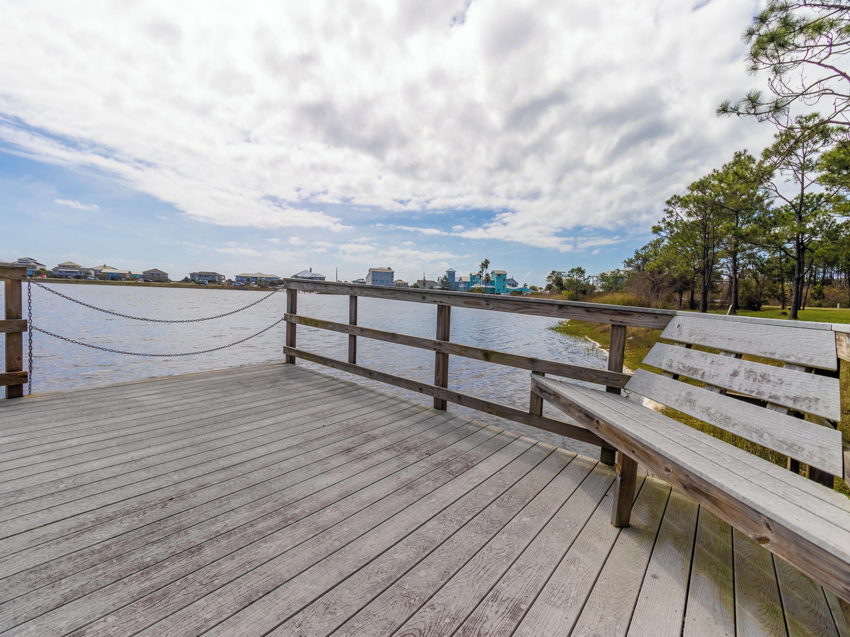 A wooden pier with a bench, a chain barrier, and a view of a distant shoreline with buildings.