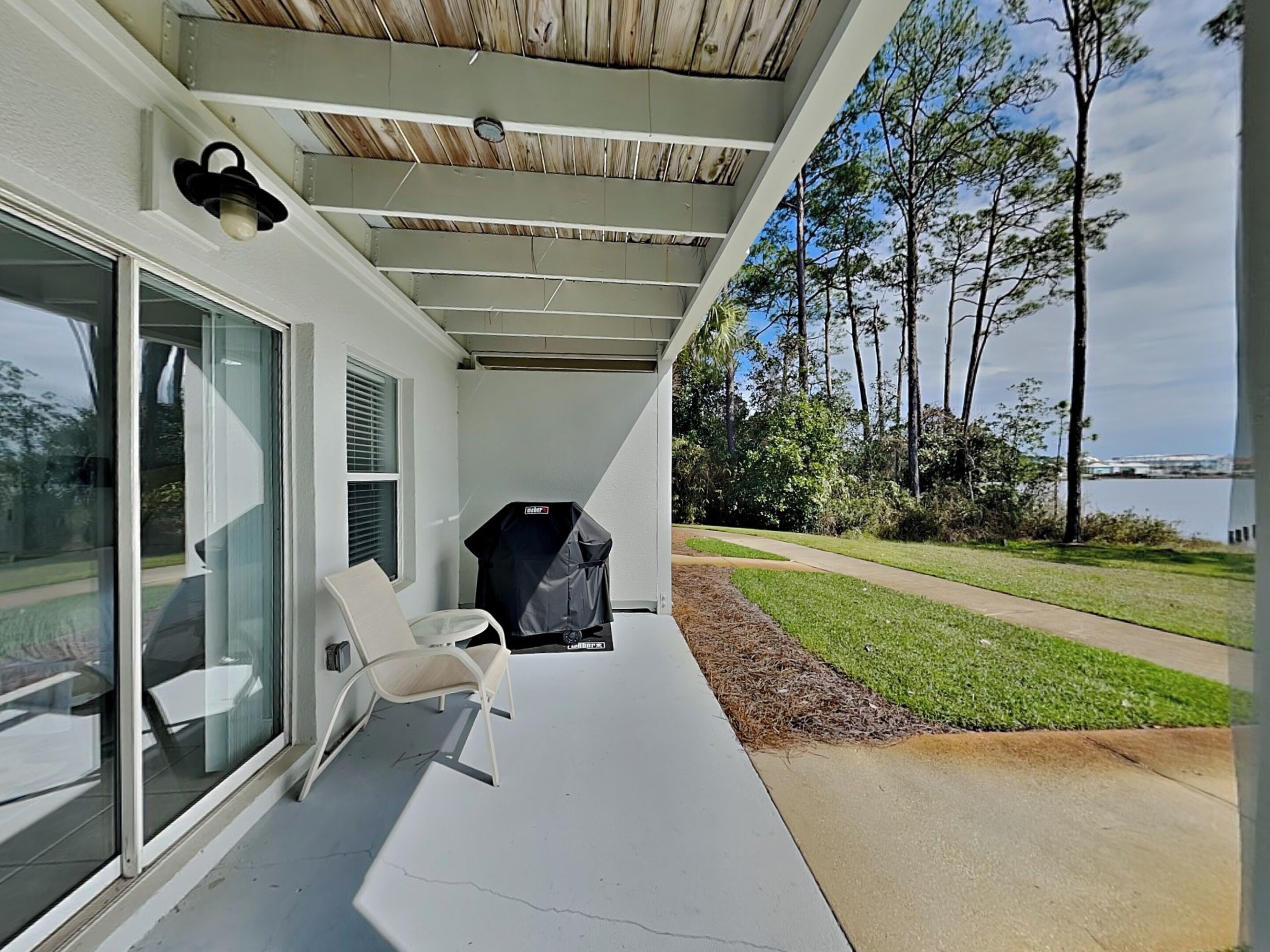 A covered patio with a grill, a chair, and a view of the water and trees.