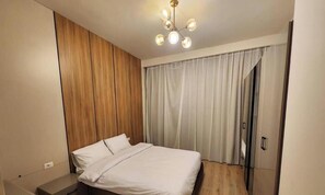 Une chambre à coucher avec un lit, un mur recouvert de panneaux en bois, un luminaire au plafond et une fenêtre avec des rideaux.