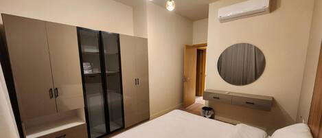 A bedroom with a bed, wardrobe, mirror, and air conditioning unit.