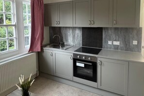 A kitchen with grey cabinets, a stainless steel sink, a black oven, and a window with a view of greenery.