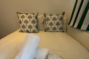 A bed with two pillows featuring a palm tree pattern, a white blanket, and a striped pillowcase.