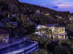 Une maison moderne avec une piscine, entourée d’arbres et de collines.