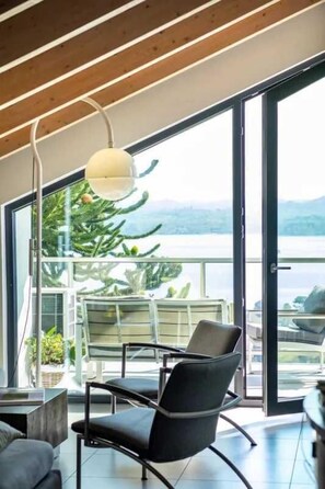 A modern interior with a large window, a black chair, and a hanging light fixture. - Maggiore Lake apartment (Lesa)