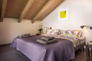 A bedroom with a bed, pillows, a bedside table, a lamp, and a framed picture on the wall. - Maggiore Lake apartment (Lesa)