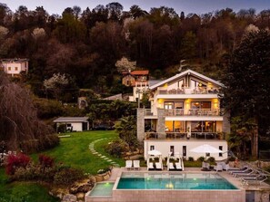 A multi-story house with a swimming pool, surrounded by a garden and forested hillside. - Maggiore Lake apartment (Lesa)