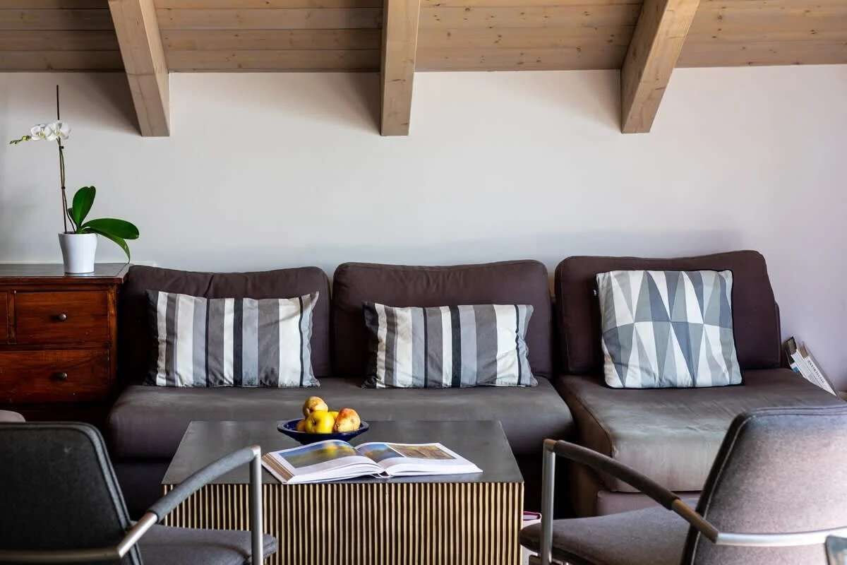 Een moderne woonkamer met een zithoek, een bijzettafeltje met een boek en fruit, en een potplant.