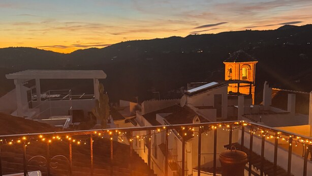 Eine Terrasse mit Feuerstelle, Geländer und Blick auf einen Hügel mit einem beleuchteten Gebäude.