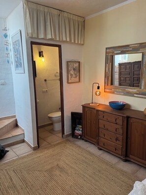 A bathroom with a toilet, a sink, and a mirror. There is a wooden cabinet with drawers and a blue bowl on top. A framed picture hangs on the wall, and a rug is on the floor. - Casa Del Panadero - Stunning Views & Sunset (Frigiliana)