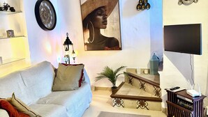 Ein Wohnzimmer mit einer Couch, einem Couchtisch, einer Pflanze, einem an der Wand befestigten Fernseher und einer Treppe.