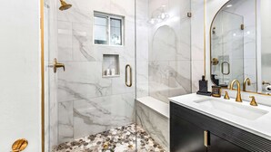 Un baño con ducha, tocador y un espejo grande.
