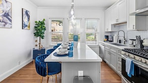 Una cucina moderna con mobili bianchi, un'isola centrale, sedie blu e un lampadario.