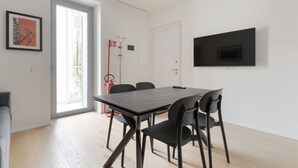 Ett modernt rum med ett matbord, stolar, en tv som är monterad på väggen och en dörr som leder ut till en balkong.