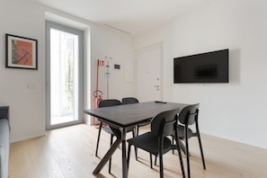 A modern room with a dining table, chairs, a TV mounted on the wall, and a door leading to a balcony. - GuestHost - Cozy 46m2 apartment, ideal for 2 people, located on the second floor of a building with lift.The accommodation is located in the Porta Romana district in a strategic position, inside municipality 4, a stone's throw from the M3 Porta Romana  (Milan)