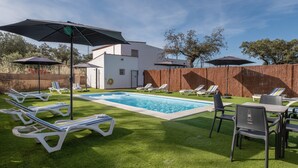 Ein Poolbereich mit Liegestühlen und Sonnenschirmen, ein weißes Gebäude und eine Holzlattenzaun.